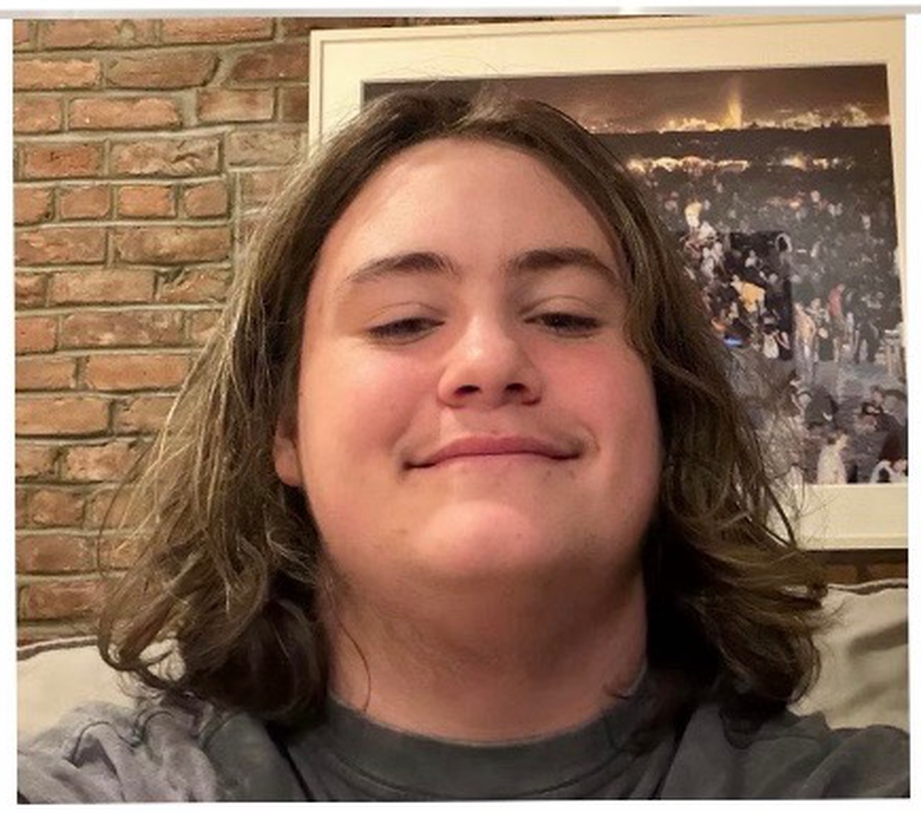 Jude Beckman, a high-school senior with shoulder-length hair, smiling in front of a brick wall.